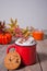 Red mug of hot creamy cocoa with froth on the wooden table with cookies, autumn leaves, candle and pumpkin on the background