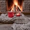 Red mug with hot tea, and a candle , wool scarf, near cozy fireplace, hygge, home sweet home