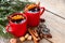 Red mugs of hot mulled wine with spices and Christmas tree branches covered with snow. Copy space for text.