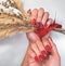 Red nails with a burgundy gradient on the background of a yellow twig with a red bow.