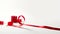 a red narrow festive ribbon elegantly arranged on a reel against a white plain paper background, for