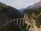 Red narrow gauge traincrossing over a stone bridge on a curvy stretch of track in the Swiss Alps.