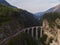 Red narrow gauge traincrossing over a stone bridge on a curvy stretch of track in the Swiss Alps.