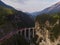 Red narrow gauge traincrossing over a stone bridge on a curvy stretch of track in the Swiss Alps.