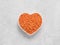 Red orange lentil Football in heart bowl on gray cement background