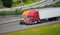 Red orange semi trucks trailers driving highway road together