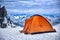 Red orange tent in a solitary bivouac in the snow atop a mountai