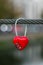 Red padlock on a rope, bokeh of evening city lights. Symbol of love. Romantic concept. Metal heart on a cable on river bridge. Hea