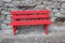 Red painted wooden bench standing on a stone pavement, rough wall with natural rocks