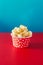 Red paper cup with popcorn against vibrant background.