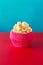 Red paper cup with popcorn against vibrant background.