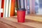 Red paper cup to takeaway on wooden floor outside the cafe. Surfing boards stand behind at the background.