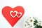 Red paper heart, two carved wooden hearts on it and white chrysanthemums on white background with copy space.
