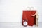 Red paper shopping bags with classic alarm clock and wooden dummy in a proposing pose on white brick wall background. Copy space