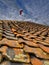 Red paraglider soaring above a traditional red-tile rooftop under a partly cloudy sky in a scenic flight, adventurous outdoor