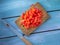 Red pepper, cut into small cubes, lies on a small wooden board on a blue rustic table