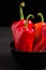 Red peppers in plate on black background - closeup photo of whole fresh ripe sweet vegetables in modern dark mood style for