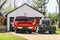 Red pickup truck and older red truck with welder on the back parked in the driveway in front of a residential garage and house
