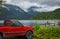 Red pickup truck parked on a lakeside with mountains in background on early moody morning. Beautiful natural landscape