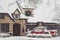 Red pickup utility vehicle parked in front of house decorated for Christmas in the snow with laturns and wreath