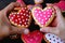 Red and pink dotted heart shaped cookies in couple`s hands put together on heap of colorful cookies