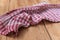 A red plaid kitchen towel lies on the countertop of a wooden table. Crumpled Towel or kitchen napkin on rough boards. Close-up.