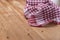 A red plaid kitchen towel lies on the countertop of a wooden table. Crumpled Towel or kitchen napkin on rough boards. Close-up.