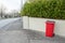 Red plastic wheelie bin out in a street ready for collection by a white fence. Urban waste management concept