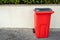 Red plastic wheelie bin out in a street ready for collection by a white fence. Urban waste management concept