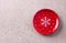 Red plate with white polka dots with a snowflake on light beige textured background, top view. Simple christmas background with