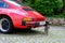 Red Porsche car parked near house in historic district old european city, young cat whiskas color sits on square, concept survival