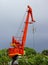 Red port crane on the background of cloudy sky and green woods.