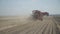 Red potato harvester travels across field and dusty.