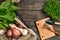 Red potatoes on burlap, garlic with greenery and a garden spade and rake on a wooden brown background