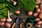 Red potatoes on burlap, garlic with greenery and a garden spade and rake on a wooden brown background