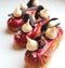 Red raspberry eclairs with meringues and chocolate decorations on light background