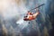 Red rescue helicopter extinguishes a forest fire by dropping a large amount of water on a burning coniferous forest