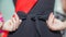 Red ribbon and belt of a schoolgirl close-up. The girl`s hands tie the belt with a bow, back view. Elements of strict school