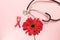 Red ribbon, red gerbera flower and a stethoscope on a pink background. The concept of medicine and human health care. World breast