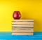 red ripe apple lies on a stack of books, yellow background