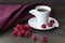 Red ripe raspberries  next to them there is a white cup of vitamin tea and red textile on wooden background,