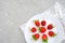 Red ripe strawberries berry on white plate, cutlery and red alarm clock on gray stone background table. Top view, flat