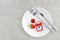 Red ripe strawberries berry on white plate, cutlery and red alarm clock on gray stone background table. Top view, flat lay, copy