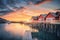 Red rorbu on wooden piles on sea coast, small jetty, orange sky