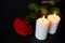 Red rose and burning candles over black background