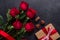 Red rose flowers bouquet, gift box, chocolate sweets on black stone background Valentine`s day greeting card