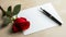Red rose and a pen on a white sheet of paper on a wooden table