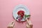 Red rose on white dish,Couple ring inside, with hand holding fork and knife, on pink background,Concept of Valentine`s Day
