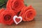 Red roses in a bouguet with a souvenir in the shape of a heart red and white color s lie on a wooden table brown. Macro.