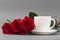 Red roses with a coffee cup of white color on a gray background